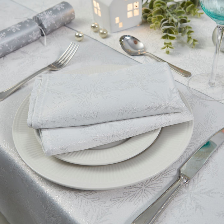 Charming napkin set with white and silver metallic snowflake patterns.