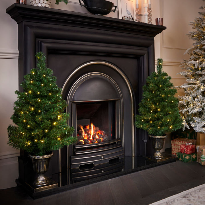 Two 3ft Christmas trees aglow with pre-lit brilliance, placed in chic pots, creating a warm and inviting atmosphere perfect for the holiday season.